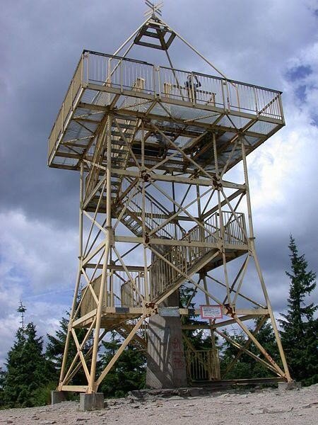 Zdjęcie przedstawia stalową konstrukcję, na szczycie znajduje się rampa do której prowadzą schody. Wieża znajduje się na szczycie góry, jest to wieża triangulacyjna i widokowa znajdująca się na Baraniej Górze. Wieża zwieńczona jest metalową częścią przypominającą krzyż. 