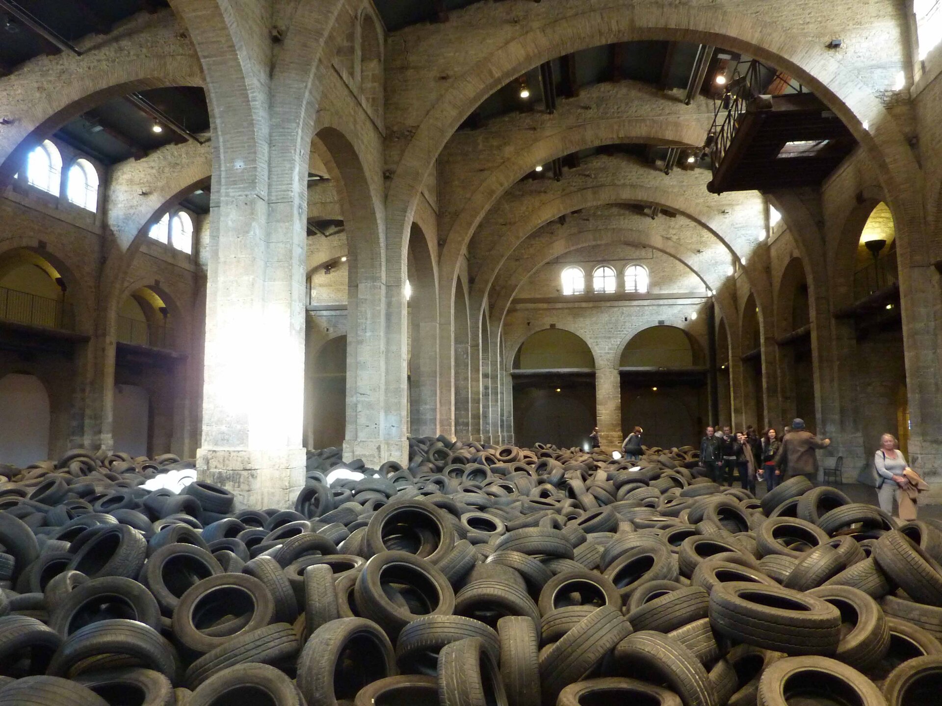 W wielkiej hali z filarami i łukowymi sklepieniami artysta Allan Kaprow umieścił na posadzce setki zużytych opon. Z góry małymi okienkami sączy się światło, z boku niewielka grupa ludzi stara się przejść. Akcja nosiła tytuł „Yard” („Dziedziniec”), 1961/2012 i miała miejsce w Bordeaux we Francji. 