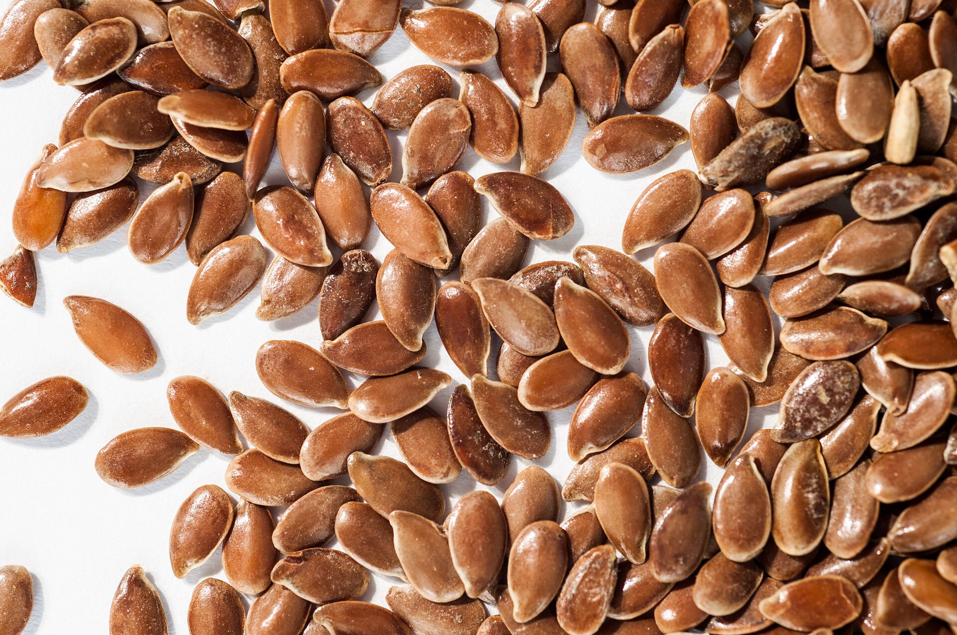 Zdjęcie przedstawia nasiona lnu. Są brązowe, małe. Mają kształt łez. Są stosunkowo płaskie.