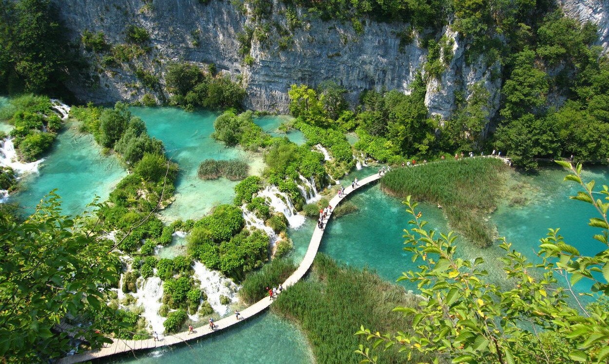 Fotografia druga wykonana z wysokości prezentuje jeziora koloru niebiesko-zielonego, połączone niskim wodospadem. Wzdłuż wodospadu poprowadzony jest kręty deptak, po którym chodzą ludzie. Na jeziorze rosną krzewy. Jeziora umiejscowione są przy skale obrośniętej roślinnością koloru zielonego. 