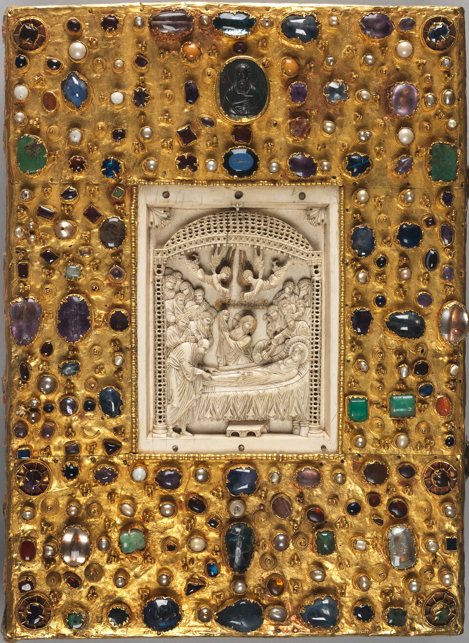 Bogato zdobiona średniowieczna oprawa księgi ze złota, wysadzana licznymi kamieniami szlachetnymi i perłami w różnych kształtach i kolorach. W centrum znajduje się prostokątna płaskorzeźba z kości słoniowej przedstawiająca scenę Zaśnięcia Matki Bożej, z postaciami otaczającymi łoże i aniołami ponad nimi. Złote tło oprawy pokrywają nieregularnie rozmieszczone gemmy, kaboszony i filigranowe detale, podkreślające ceremonialny charakter dzieła.