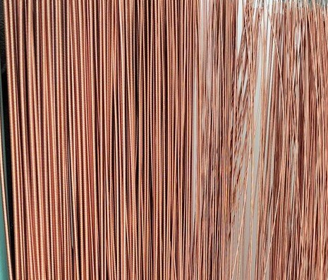 Zdjęcie przedstawia struny basowe wykonane z drutu miedzianego nawiniętego na rdzeń z drutu stalowego. Widoczne są struny zawieszone w pękach.