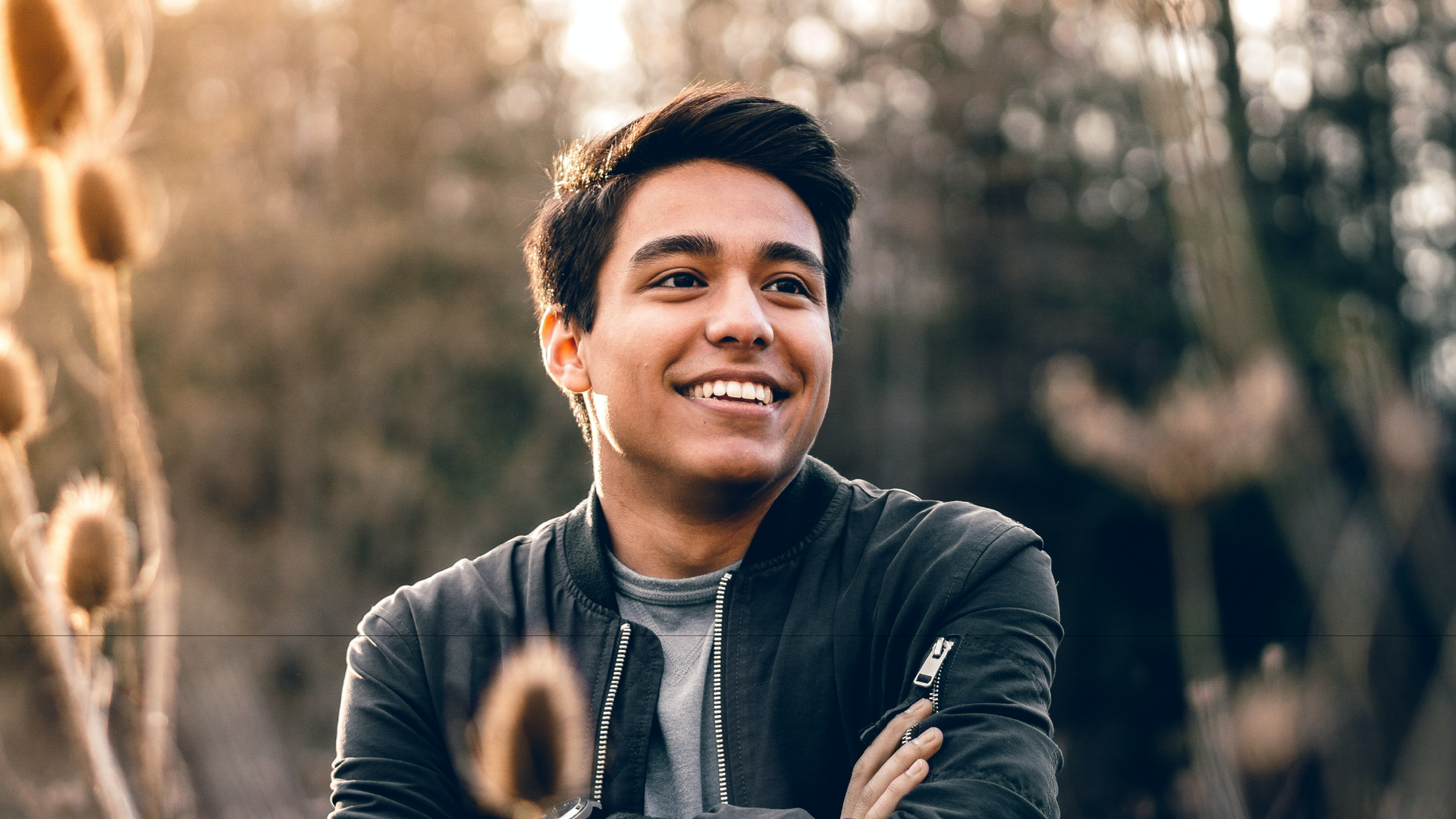 Zdjęcie przedstawia młodego mężczyznę z bardzo szerokim uśmiechem, widoczny jest górny rząd jego zębów. Oczy ma wpatrzone w dal.