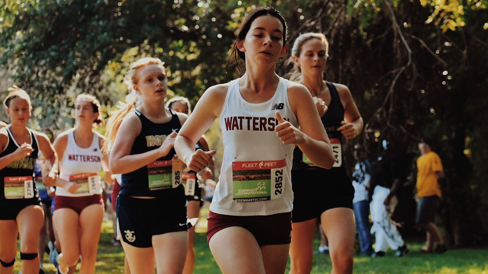 Zdjęcie przedstawia grupę kobiet w strojach sportowych biegnące w jednym kierunku. Na koszulkach mają naklejone kartki z numerami. 