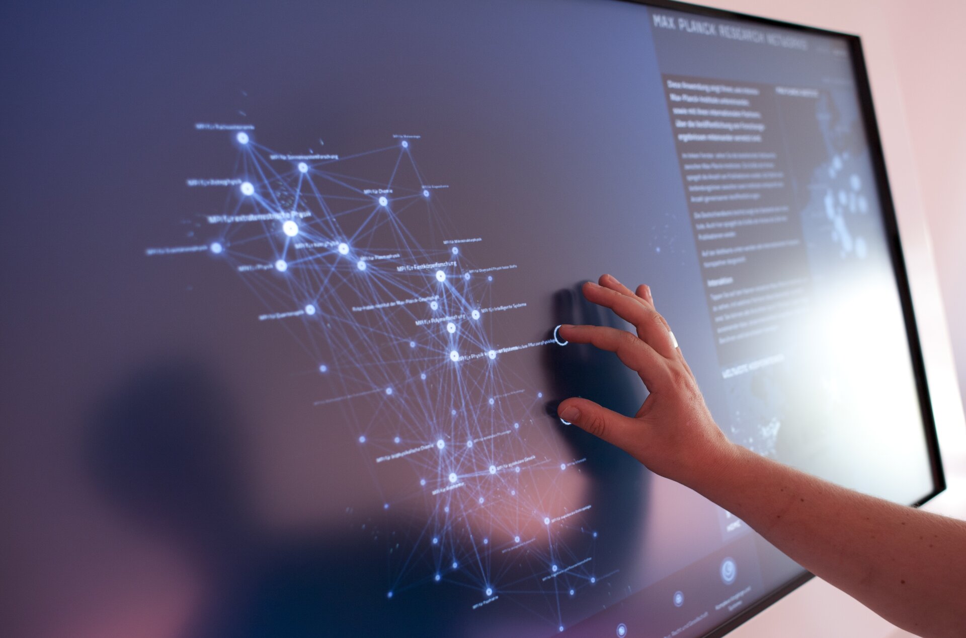 Ilustracja przedstawia postać posługującą się ekranem dotykowym, który stanowi element wystawy Max Planck Science Gallery