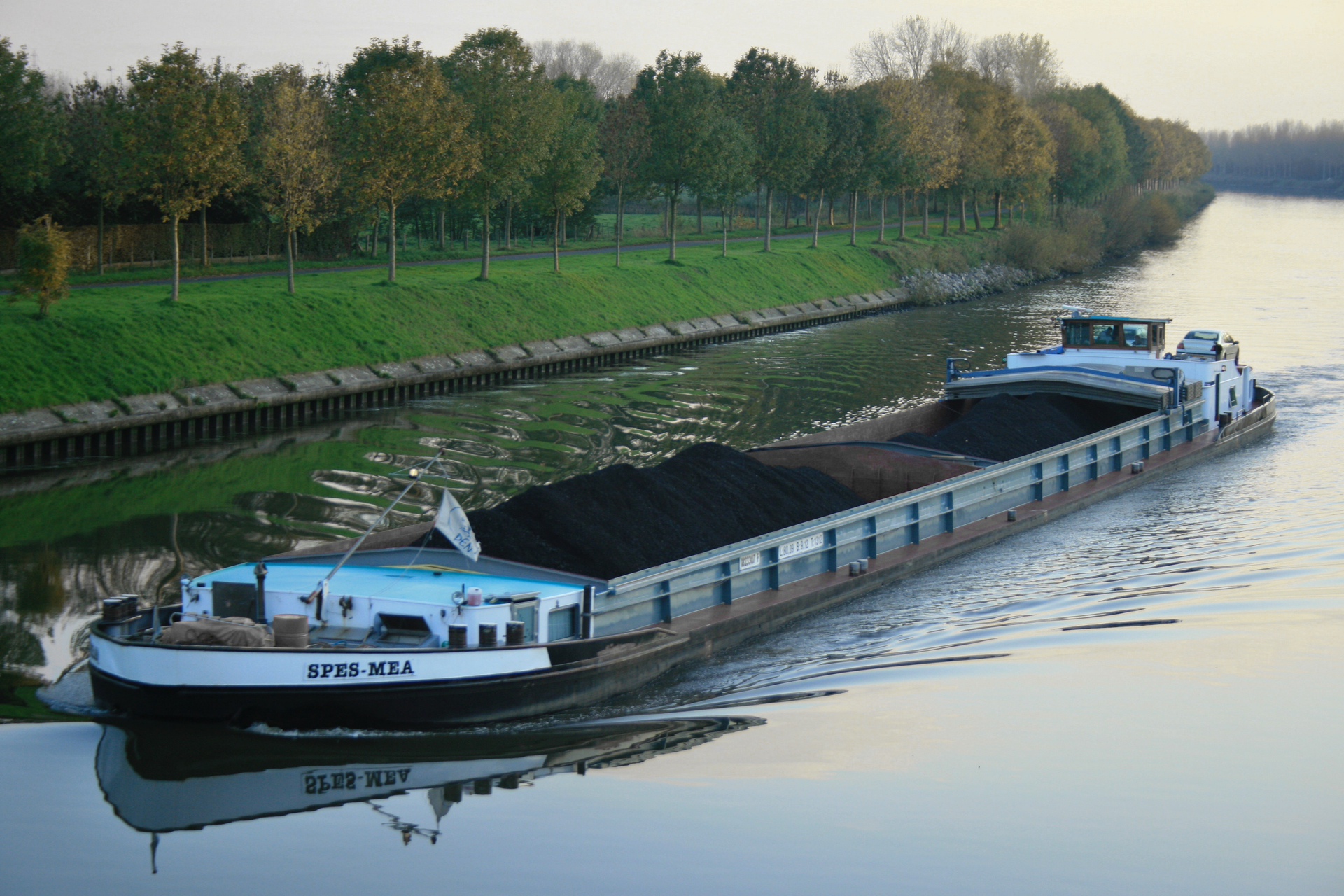 Zdjęcie przedstawia statek masowiec. Płynie on po rzece. Przewozi on hałdy węgla.