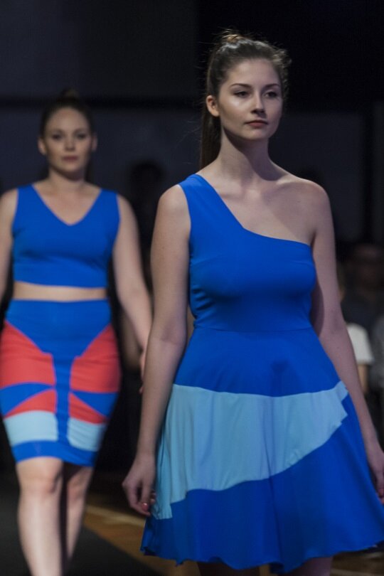 Zdjęcie przedstawia dwie modelki prezentujące ubrania: jedna ma na sobie sukienkę, druga komplet składający się z topu i spódnicy, oba są w niebieskim kolorze.