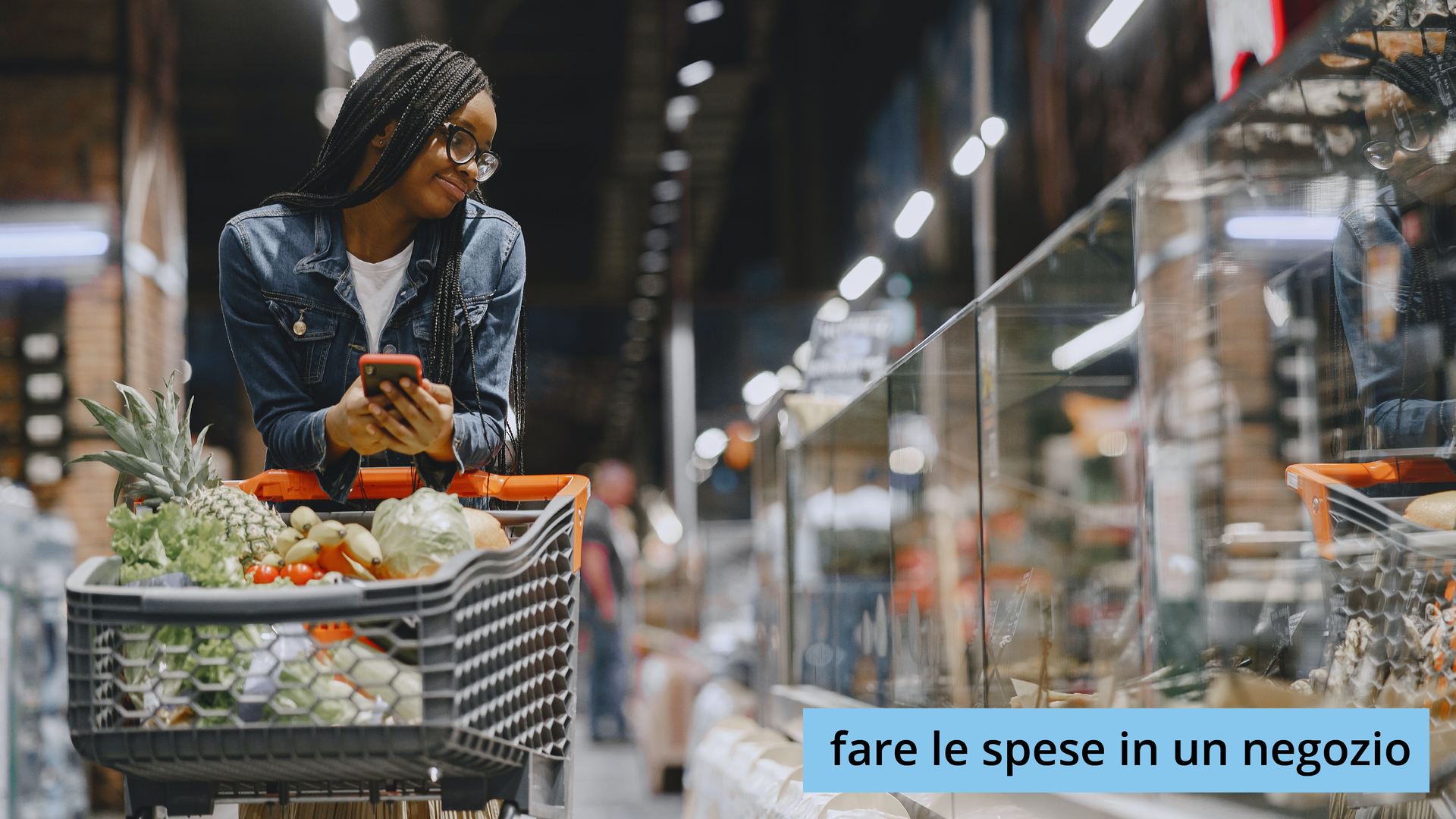 Zdjęcie przedstawia kobietę w okularach, która robi zakupy w sklepie. Kobieta w ręku ma telefon komórkowy, a przed sobą wózek wypełniony po brzegi zakupami spożywczymi. Kobieta spogląda co znajduje się w ladzie. Na ilustracji widoczny jest napis: fare le spese in un negozio.