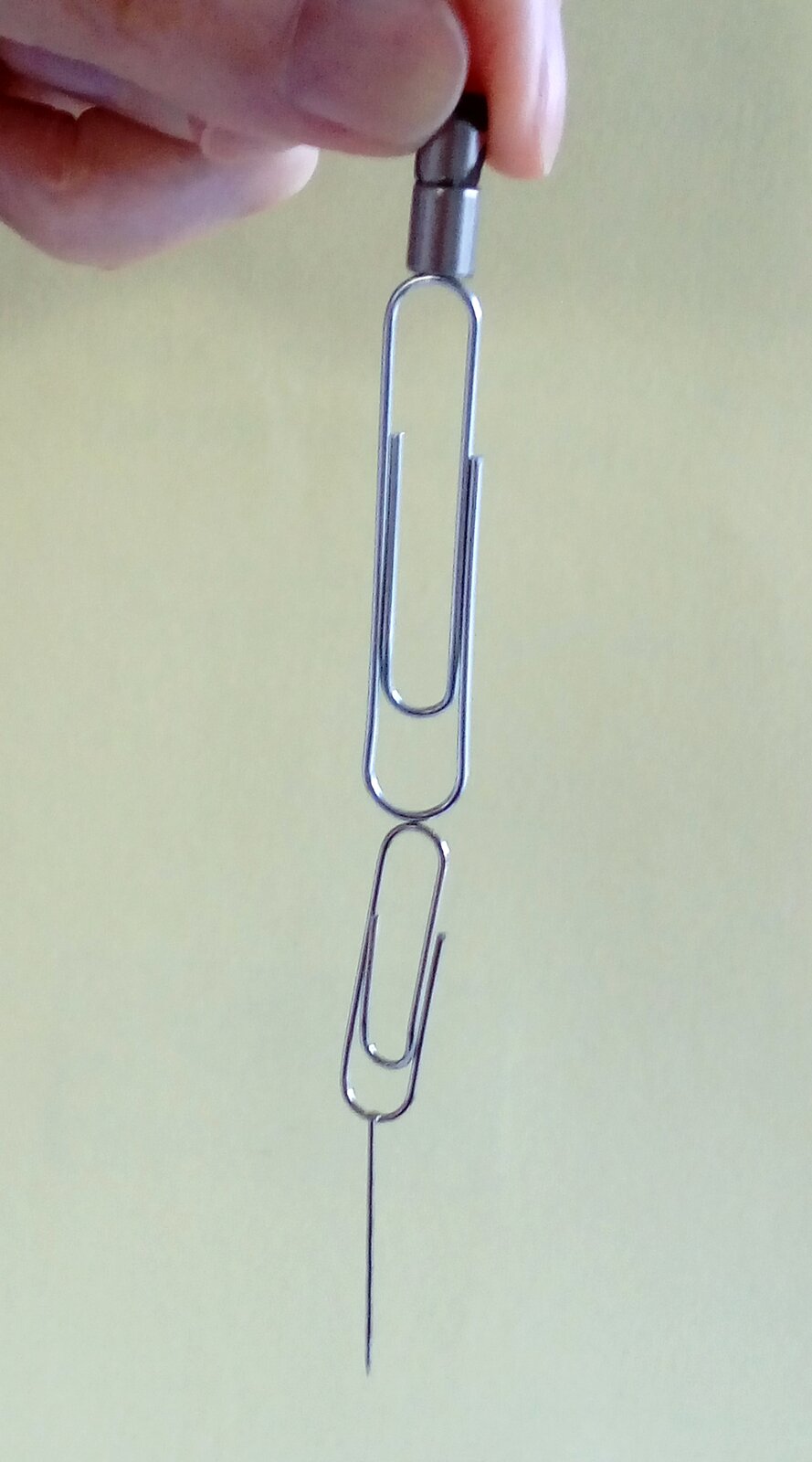 Rys. b. Zdjęcie poglądowe przedstawia dłoń trzymającą magnes, do którego przyczepiony jest duży spinacz, a potem kolejno do spinacza przyczepiony jest mniejszy spinacz i na końcu szpilka.