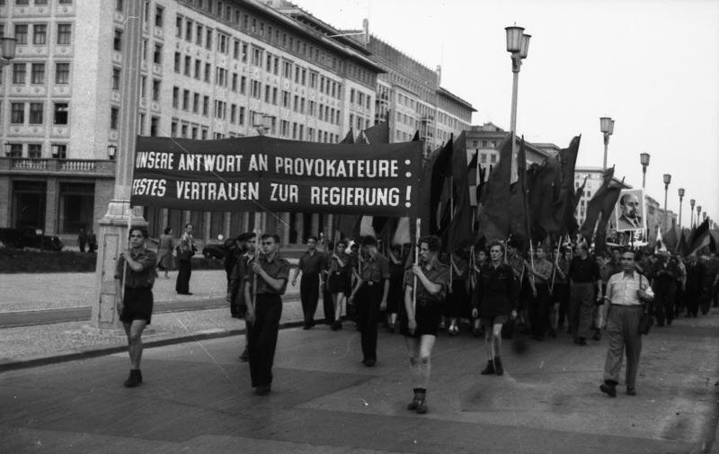 Zdjęcie przedstawia demonstrację w Berlinie Wschodnim 26 czerwca 1953 roku. Szeroką ulicą idzie pochód. Są tu młodzi ludzie. Na czele pochodu maszeruje trzech młodych mężczyzn, którzy trzymają duży transparent w języku niemieckim (w tłumaczeniu „Nasza odpowiedź na prowokację: mocne zaufanie dla rządu!”). 
