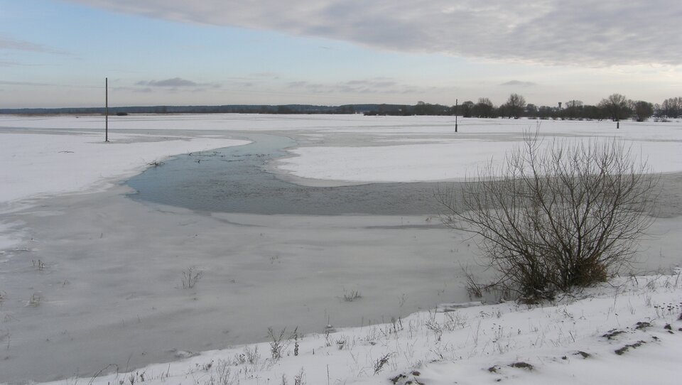 Zdjęcie przedstawia zimowy krajobraz oraz zakole zamarzniętej rzeki. 
