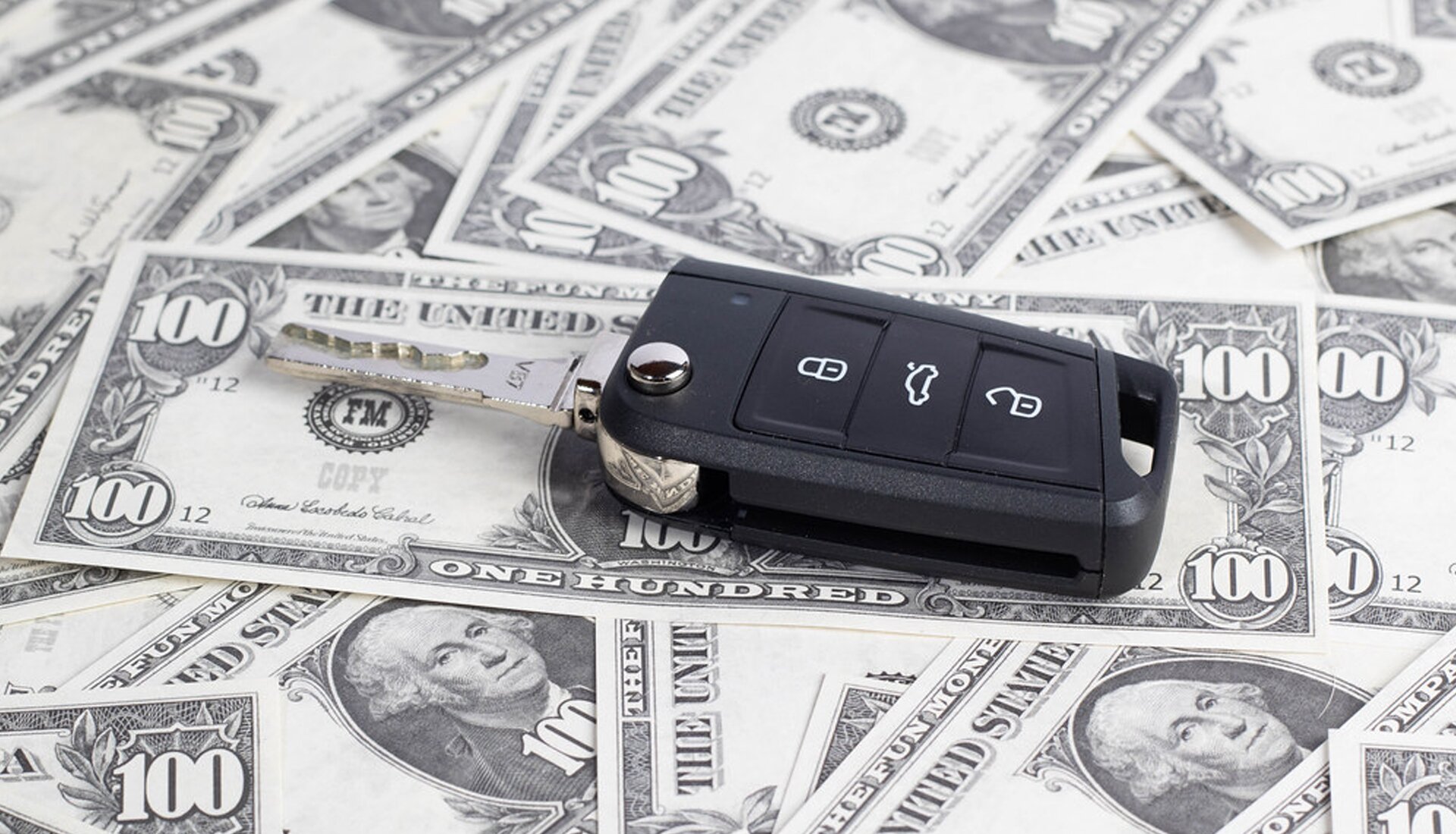 Zdjęcie przedstawia kluczyk do samochodu leżący na banknotach studolarowych.