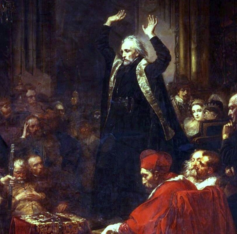 Fragment obrazu przedstawiający starszego mężczyznę ukazanego lewym profilem. Jego twarz jest szczupła, pociągła, oczy ma głęboko osadzone, nos spiczasty. Ma sporą łysinę, siwe, rozwichrzone, półdługie włosy, krótką brodę i wąsy. Mężczyzna ubrany jest w czarną sutannę i płaszcz ze złotą lamówką. Stoi i wznosi ręce nad głowę. Wokół mężczyzny siedzi wiele postaci: szlachcice, duchowni, zagraniczni widzowie oraz młode arystokratki. Pod nogami mężczyzny stoi kwadratowy stolik przykryty długim obrusem.