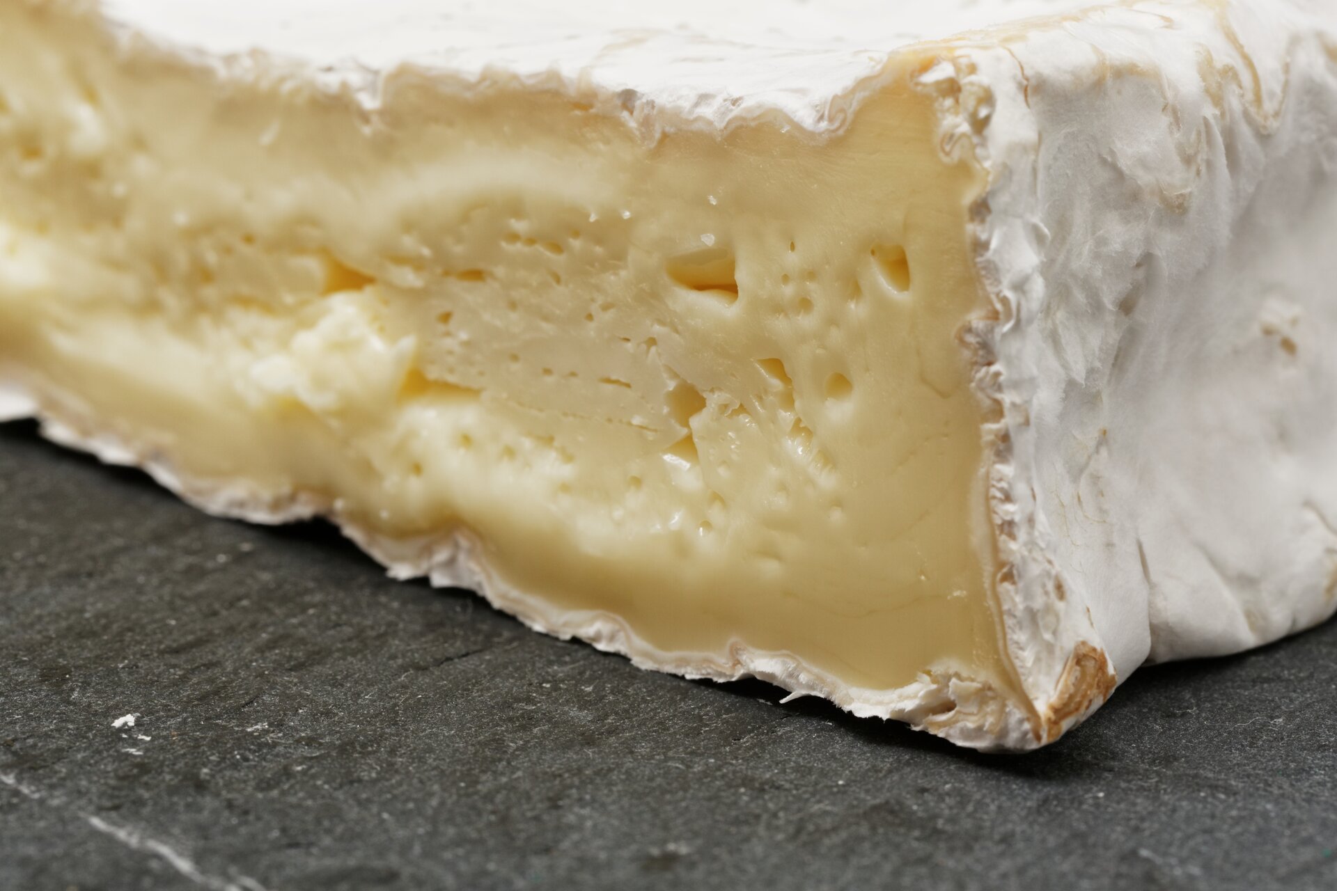 Fotografia przedstawiająca zbliżenie na kawałek sera brie. Na zewnątrz jego skórka jest biała. Środkowa część posiada maślany kolor.