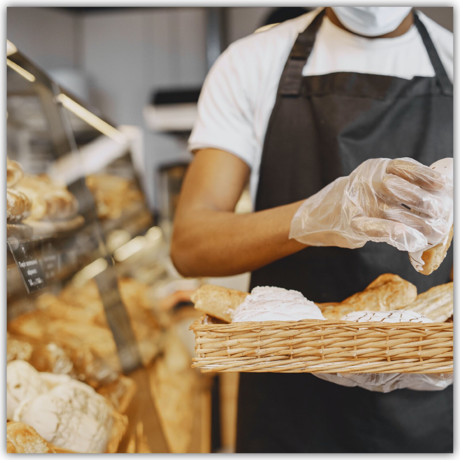 Widoczne jest stoisko z pieczywem i osoba w fartuchu która trzyma koszyk z pieczywem.