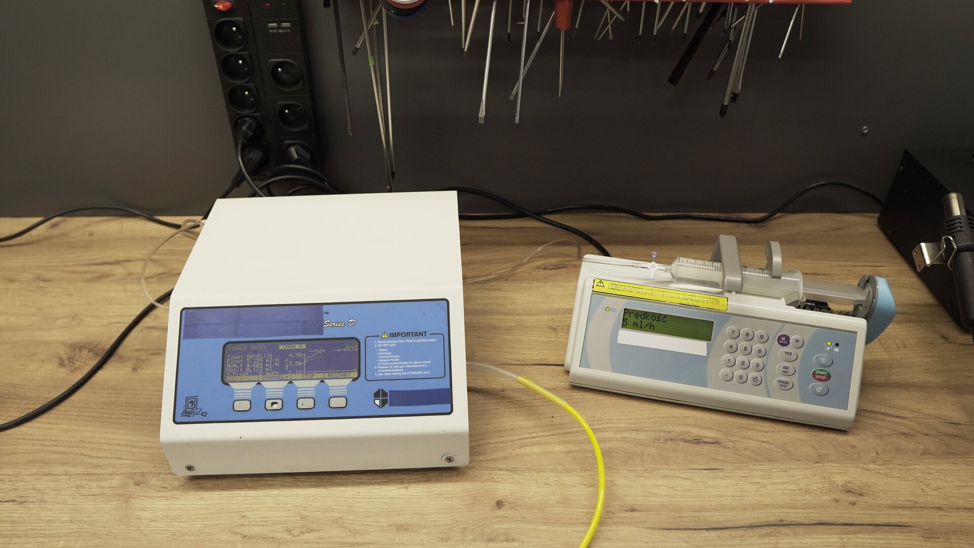 Na zdjęciu pokazane jest urządzenie testujące wraz z podłączoną pompą infuzyjną. W ramieniu pomby znajduje się strzykawka wypełniona wodą. 