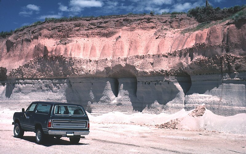 Zdjęcie przedstawia serię skalną. Na pierwszym planie znajduje się samochód. Za nim są wysokie skalne ściany o jasnej barwie z licznymi wgłębieniami.