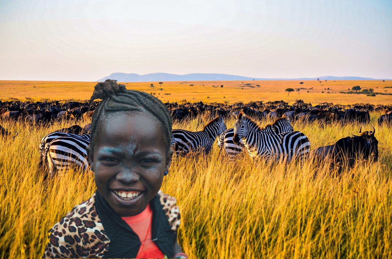 Zdjęcie przedstawia czarnoskórą dziewczynkę, widzianą od klatki piersiowej w górę, która stoi na tle sawanny. Dziewczynka ma ciemne, zaplecione w warkoczyki włosy, upięte w kok. Ubrana jest w żakiet w panterkę i czerwoną koszulkę. Ma otwarte w szerokim uśmiechu usta, lekko zmrużone oczy. W tle widoczne są żółte trawy sawanny, na której pasą się zebry.