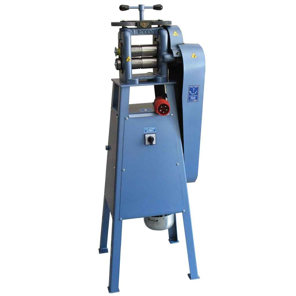 Zdjęcie przedstawia walcarkę elektryczną. To metalowe urządzenie w kształcie ostrosłupa ze ściętym wierzchołkiem, wyposażone w cztery długie nogi. Między nogami znajduje się niewielki metalowy pojemnik. Urządzenie na szczycie posiada dwa walce robocze, a nad nimi motylkowe urządzenie nastawy walców. Po prawej stronie znajdują się dwie długie, metalowe osłony. Znajdują się na nich naklejki z ostrzeżeniami. Na froncie walcarki znajduje się gniazdo do przyłącza elektrycznego oraz włącznik.