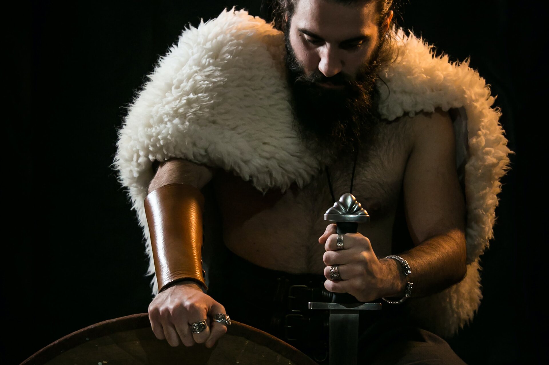 Zdjęcie przedstawia mężczyznę okrytego skórą z barana, który trzyma w dłoni miecz. 