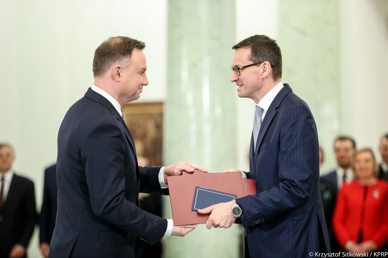 Zdjęcie przedstawia prezydenta Andrzeja Dudę, który wręcza nominację na stanowisko Prezesa Rady Ministrów Mateuszowi Morawieckiemu. W tle pracownicy Kancelarii Prezydenta.