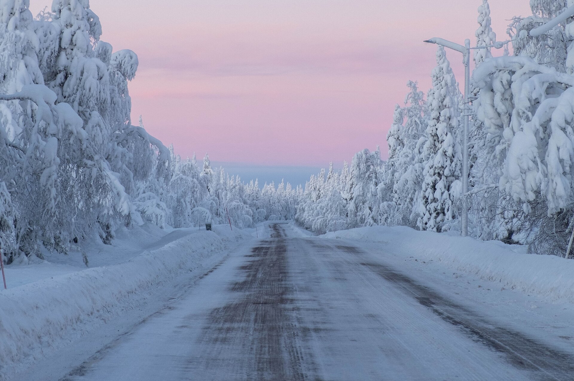 Zdjęcie przedstawia zaśnieżony krajobraz. Oblodzona droga prowadzi przez las, którego drzewa pokrywa śnieg. 