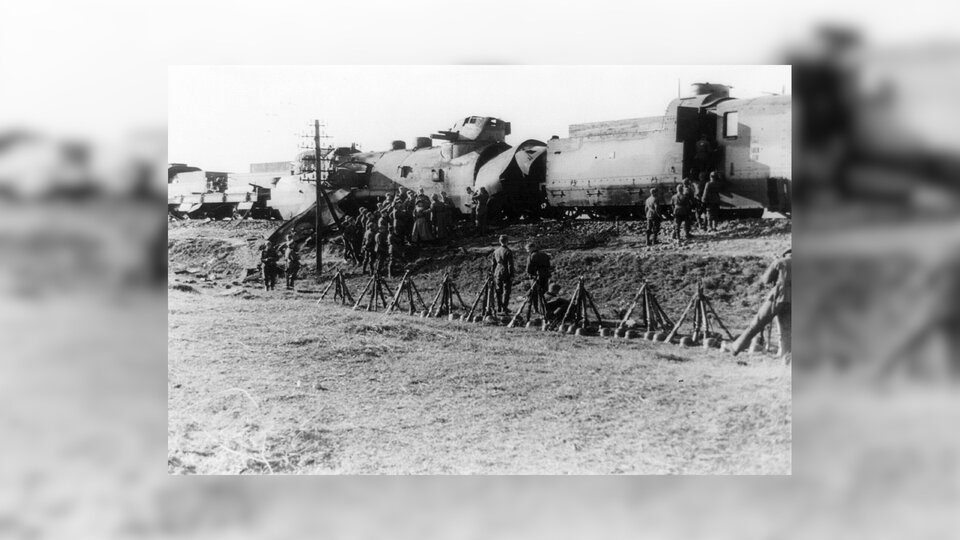 Zdjęcie przedstawia nasyp kolejowy, na którym stoi opancerzony pociąg. Przy wagonach grupy żołnierzy oraz karabiny ułożone w kształcie piramid.