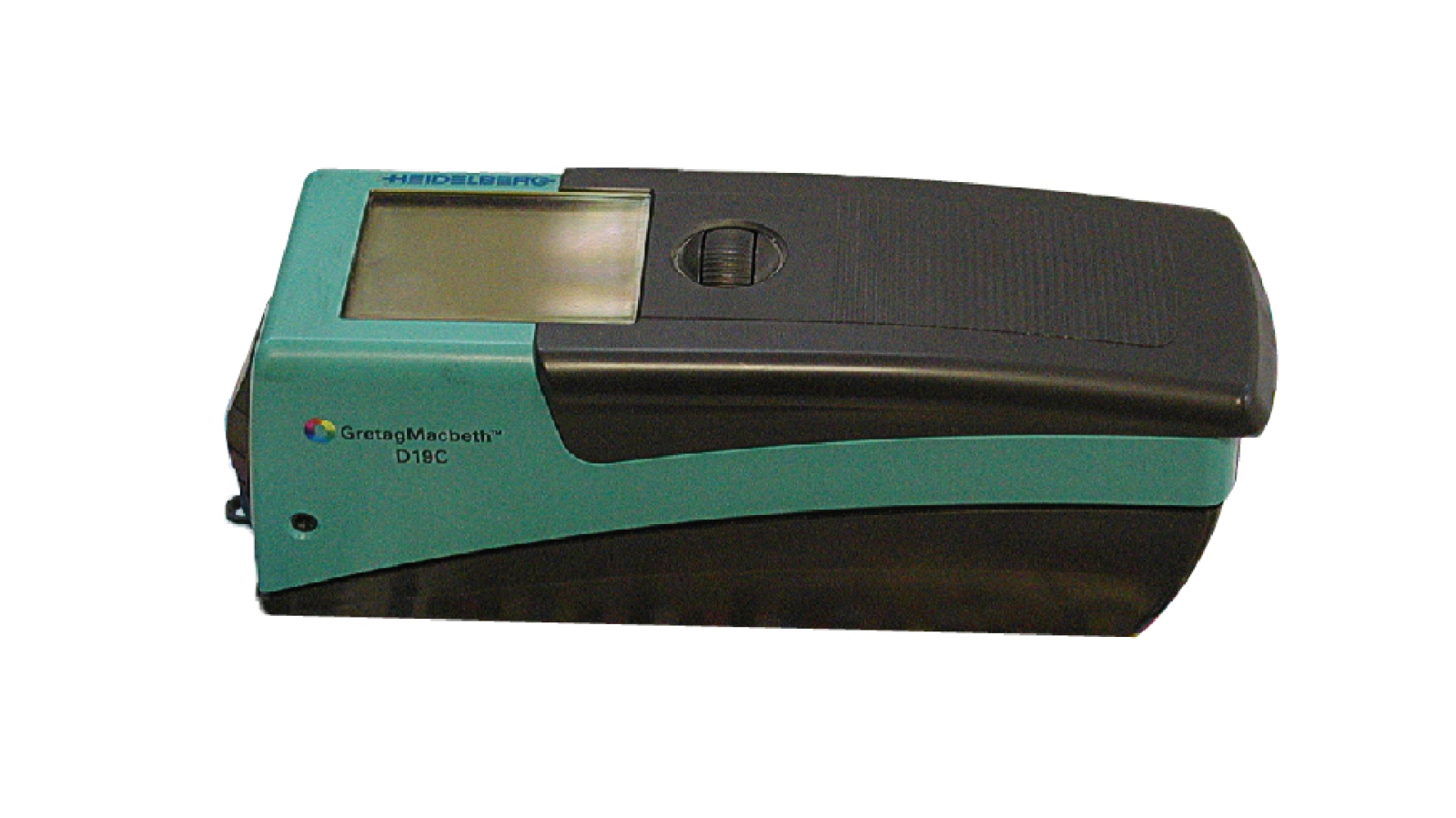 Zdjęcie przedstawia densytometr położony na wydrukach z profilami barwnymi, próbkami kolorystycznymi, skalą szarą. Widoczna jest obudowa przyrządu o prostopadłościennym kształcie, w kolorze czarnym i zielonym. Widoczny jest dłuższy bok i góra. W górnej części znajduje się wyświetlacz oraz pokrętło do jego obsługi.