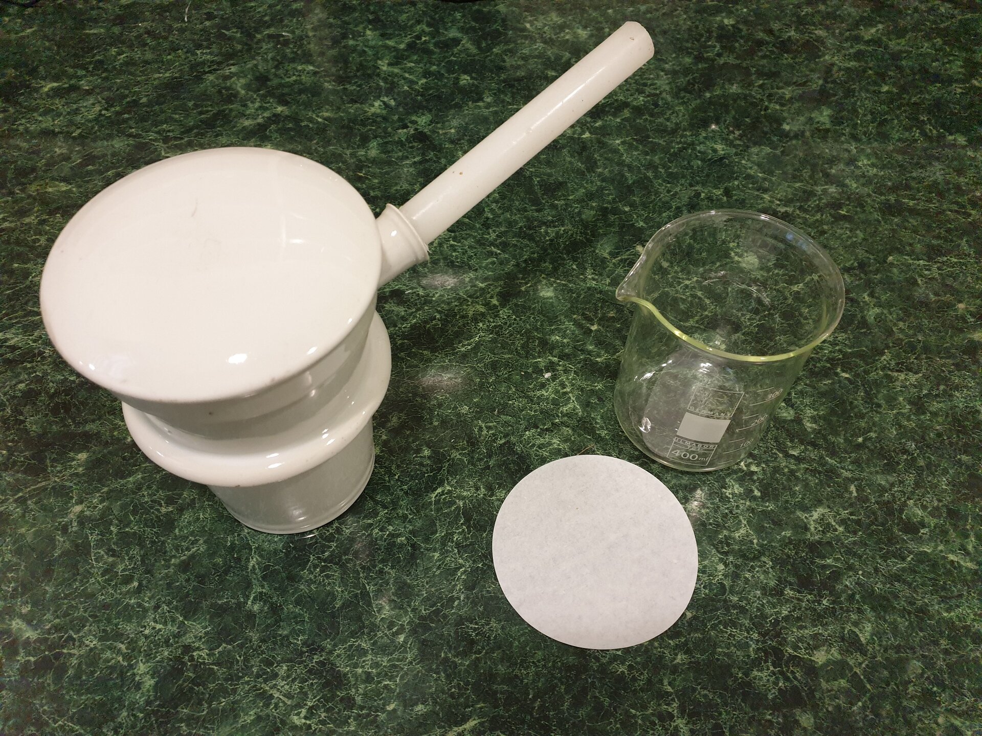 Odwary, napary i maceracje. Rycina przedstawia ceramiczną infuzorkę z rączką i wieczkiem, okrągły, papierowy filtr oraz szklane naczynie z podziałką, mające formę walca, a na górnej krawędzi wyżłobienie, które pomaga w przelewaniu. 
