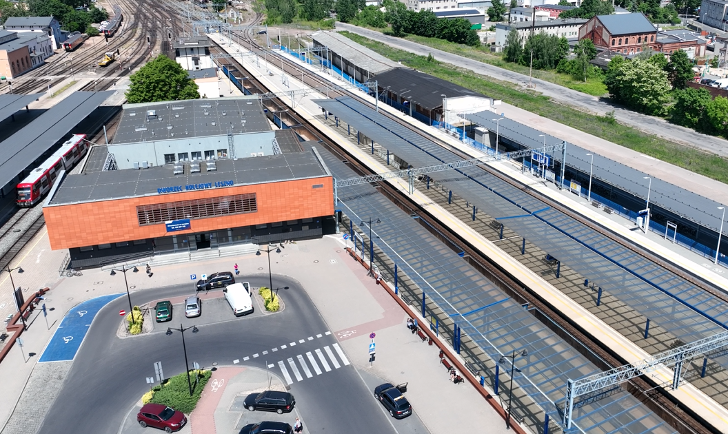 Zdjęcie przedstawia widok z lotu ptaka na dworzec kolejowy. Widoczna jest droga dojazdowa do terminala dworcowego oraz kilka miejsc parkingowych, terminal dworca oraz cztery tory z prawej i sześć torów z lewej strony, z zadaszonymi peronami umieszczonymi co dwa tory.