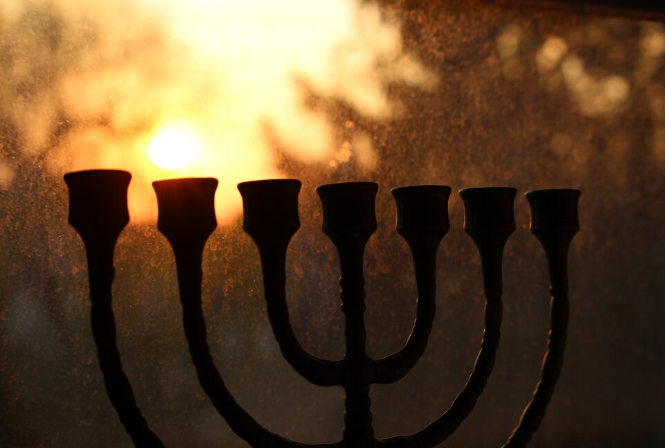 Na zdjęciu znajduje się menora - siedmioramienny, tradycyjny, żydowski świecznik. Z pionowego trzonu świecznika wychodzą trzy ramiona w lewo i trzy ramiona w prawo. Wykonany jest z metalu. 