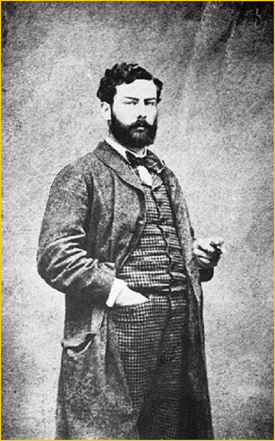 Ilustracja przedstawia Alfreda Sisleya.  Na czarno‑białej fotografii widoczny jest mężczyzna stojący w swobodnej pozie. Ubrany jest w długi, ciemny płaszcz, pod którym ma kamizelkę w drobną kratę oraz koszulę z krawatem lub fular. Jedna ręka spoczywa w kieszeni, a w drugiej trzyma niewielki przedmiot, prawdopodobnie papieros.  Tło jest jednolite i pozbawione szczegółów, co kieruje uwagę na postać. Styl ubioru oraz technika wykonania zdjęcia wskazują na drugą połowę XIX wieku.