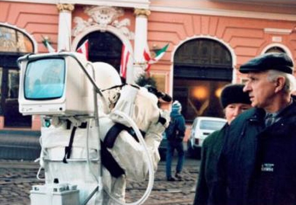 Ilustracja przedstawia pracę Pawła Althamera „Astronauta”. Dzieło pochodzi z 1995 roku. Na fotografii widzimy mężczyznę w białym kostiumie astronauty. Na plecach ma założony mały ekran. Obok astronauty przechodzi starsze małżeństwo. Bohater znajduje się w centrum miasta. W tle widoczny jest budynek, samochód oraz przechodzień. Autorem pracy jest polski rzeźbiarz, performer, twórca instalacji i filmów wideo.