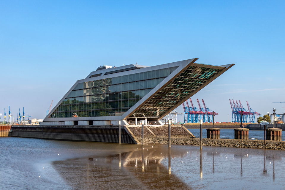 Ilustracja przedstawia szklany budynek w kształcie równoległoboku.