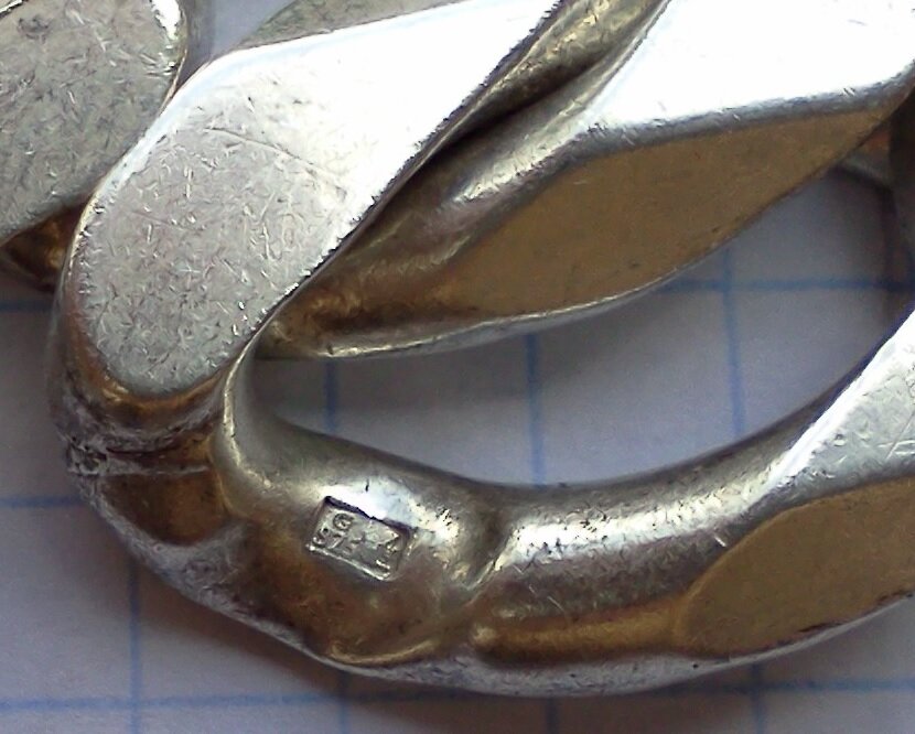 Zdjęcie przedstawiające fragment wyrobu srebrnego, który to jest ocechowany, to znaczy naniesiono na niego symbol wskazujący na jego pochodzenie oraz próbę srebra. W tym przypadku to 925.