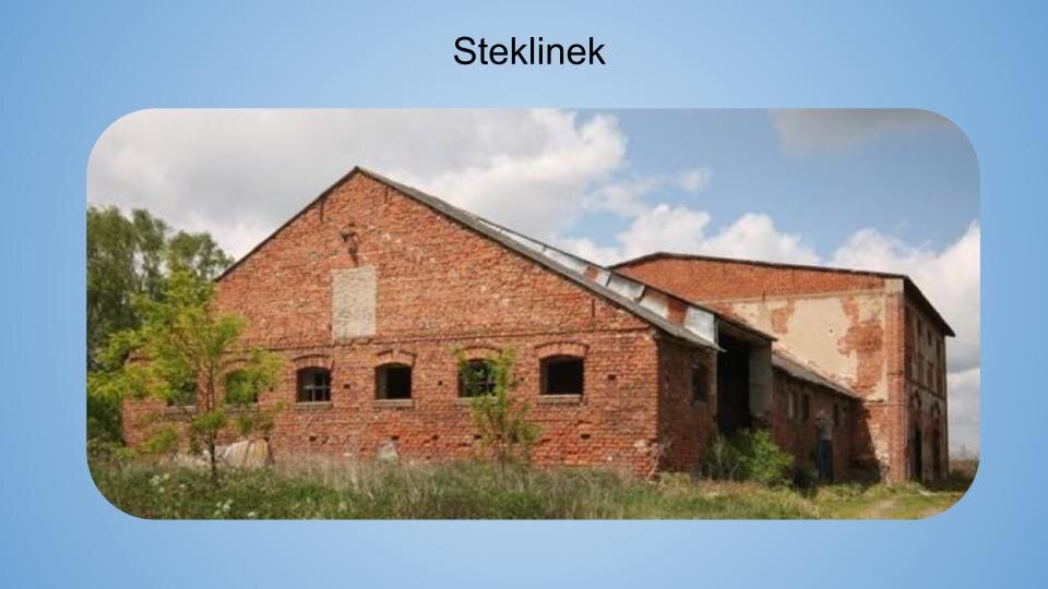 Jasnoniebieskie tło. Na górze napis: Steklinek. Poniżej kolorowa fotografia przedstawiająca duży ceglany budynek ujęty z boku. Na pierwszym planie widoczna jest boczna ściana budynku z sześcioma oknami. Dwa pierwsze okna od lewej są przysłonięte przez gałęzie niewielkiego drzewka. W trzecim oknie widoczny jest stelaż na 6 niewielkich szyb. Czwarte okno jest całkowicie pozbawione szyb. Piąte jest przysłonięte przed gałęzie drugiego drzewka. W szóstym oknie również nie ma szyb. Ta część budynku ma spadzisty dach. Na dalszym planie widoczna jest główna, wyższa część budynku o nieco bardziej wypłaszczonym dachu. Cegły częściowo pokryte są jasną, obdrapaną elewacją. Dookoła widać zaniedbaną trawę i dziko rosnącą roślinność. W tle zachmurzone niebo. Zdjęcie zostało wykonane w świetle dziennym.
