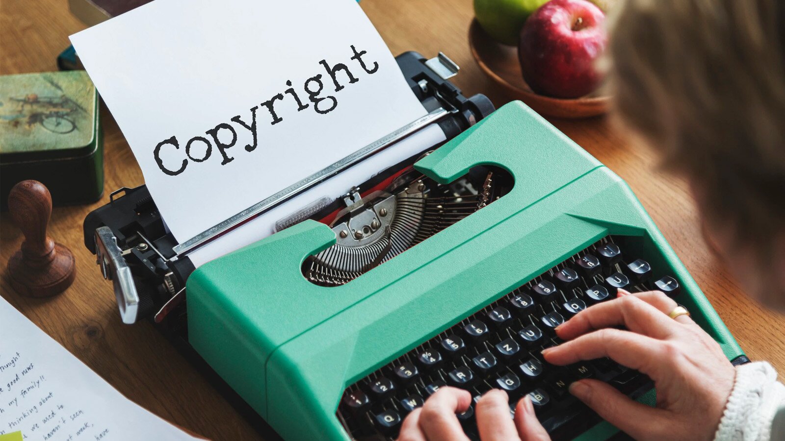 Zdjęcie przedstawia maszynę do pisania, na której ktoś właśnie pisze – nie wiemy, kto, bo w kadrze mieszczą się tylko dłonie tej osoby i kawałek głowy. W mechanizm maszyny do pisania jest wkręcona biała kartka, na której znajduje się wyraz zapisany w języku angielskim: Copyright.