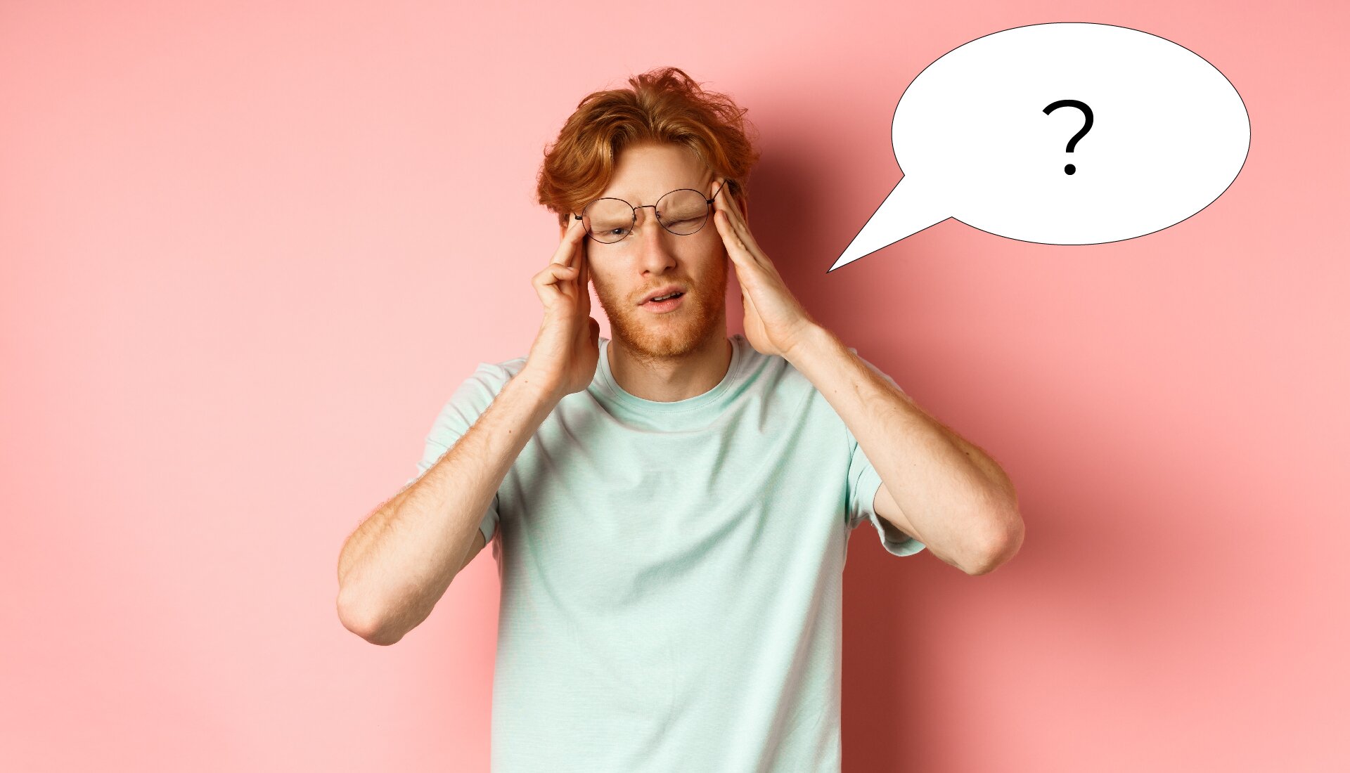 Na zdjęciu znajduje się mężczyzna w okularach i w białej koszulce, widoczny od pasa w górę, który trzyma się dłońmi za skronie.