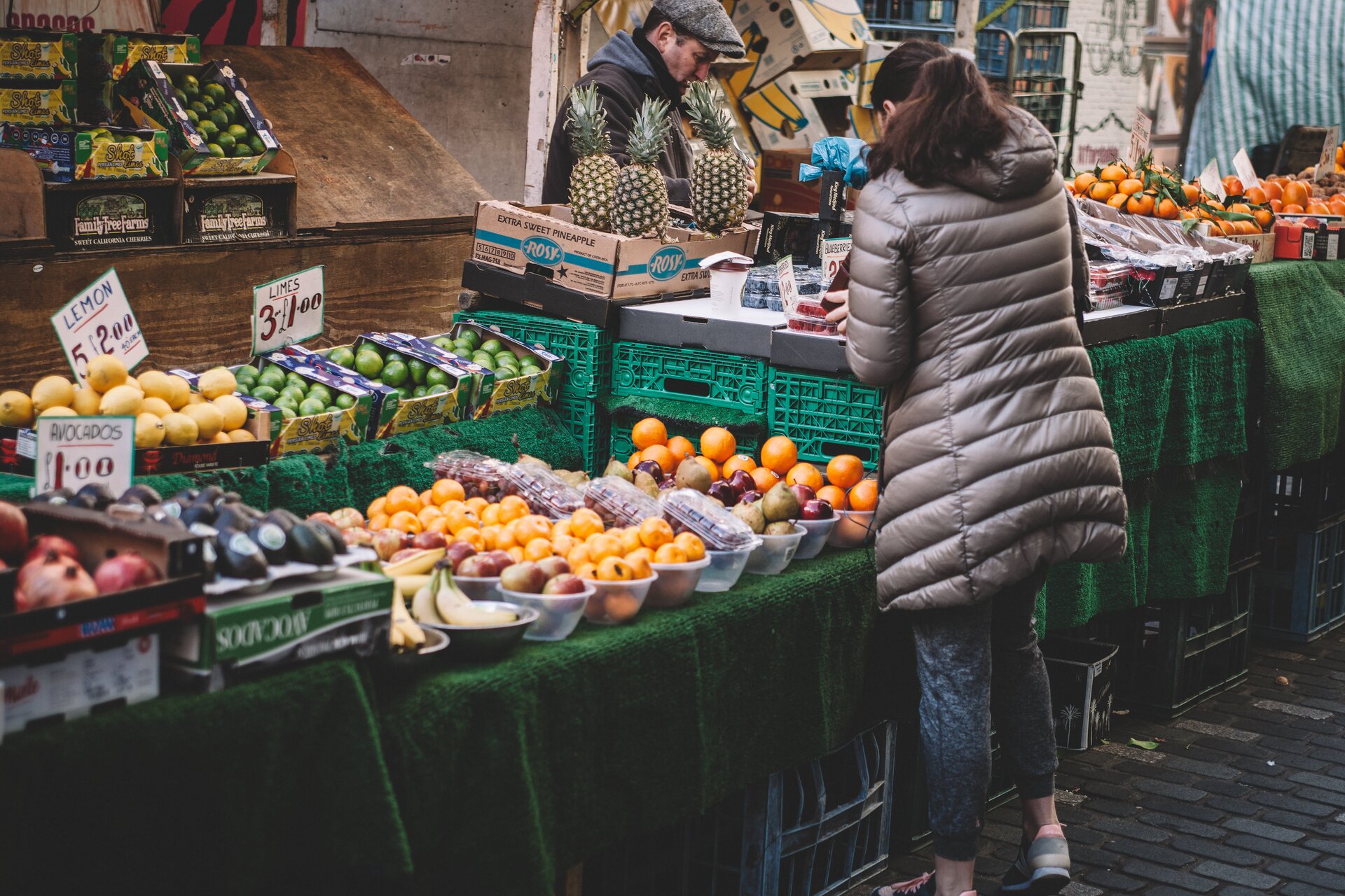 Krok piąty. Sprzedaż produktów rolnych. Przedstawione jest stoisko sklepowe, gdzie w skrzynkach znajdują się warzywa i owoce, między innymi mandarynki, ananasy, limonki, cytryny i awokado. Przy każdym produkcje ustawiona jest plakietka z nazwą i ceną.