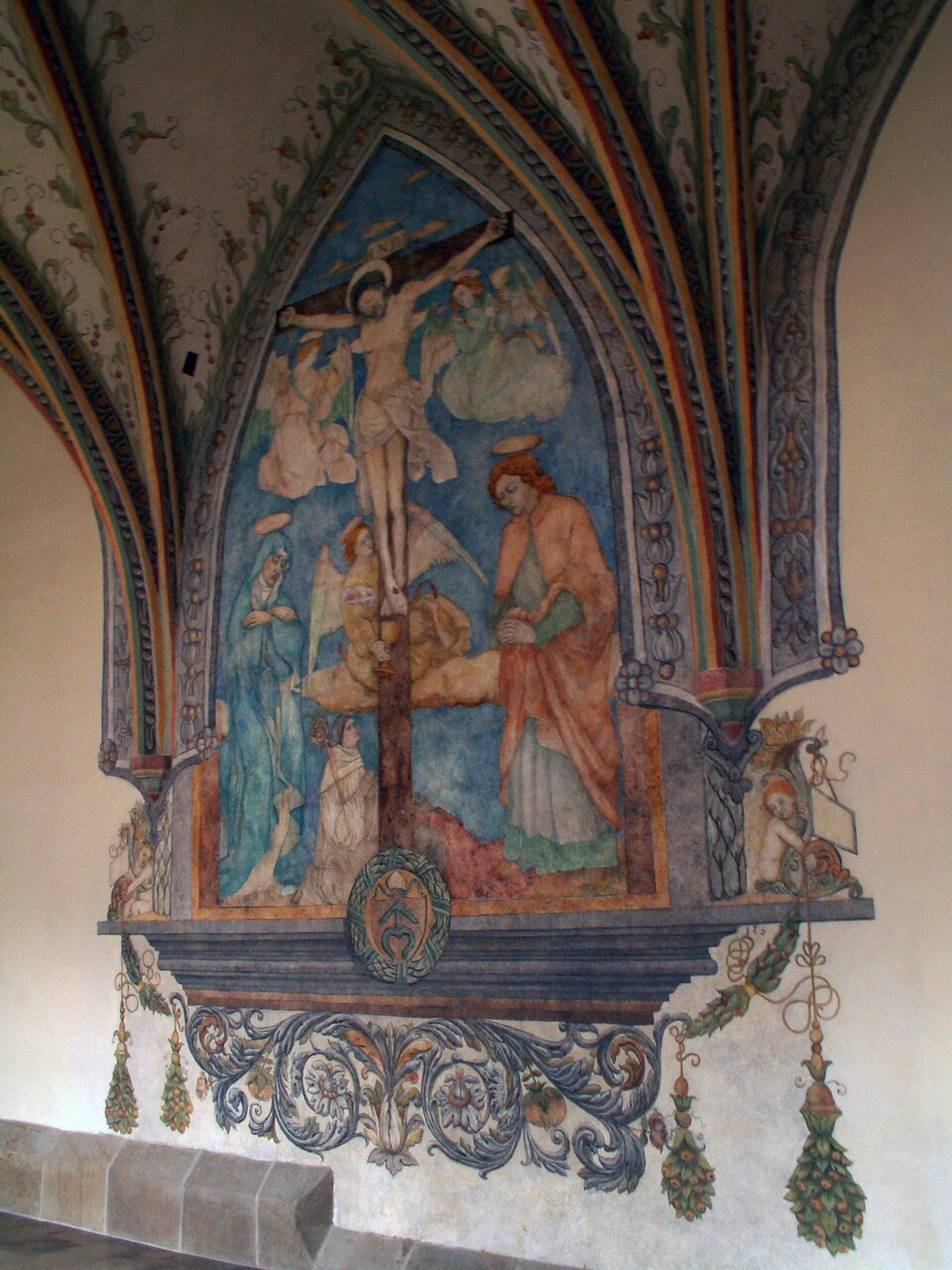 Ilustracja przedstawia fresk ukazujący ukrzyżowanego Chrystusa w otoczeniu aniołów. Dwie skrzydlate istoty unoszą się na wysokości piersi ukrzyżowanego. Obok stóp Chrystusa znajduje się trzeci anioł. Poniżej stoją dwie postaci. Po lewej stronie stoi Matka Boska. Postać pochyla głowę i załamuje ręce. Jest ubrana w obszerne szaty. Obok klęczy mężczyzna ubrany w biskupie szaty. Prawą ręką przytrzymuje pastorał. Po przeciwnej stronie stoi mężczyzna w sile wieku. Postać pochyla głowę i składa ręce do modlitwy. 