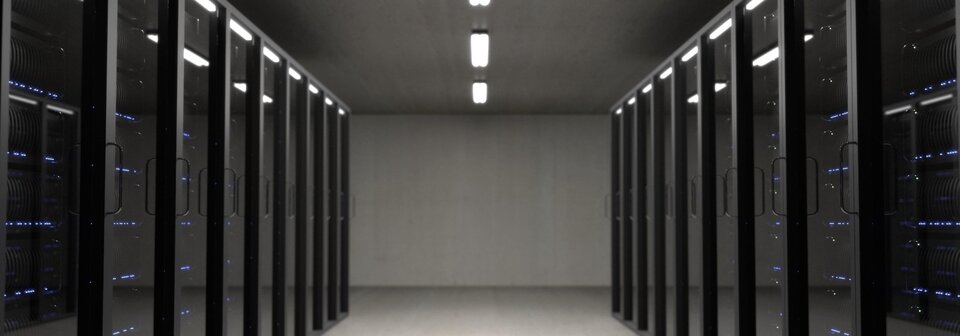 Grafika poglądowa serwerowni. Po prawej i lewej stronie grafiki widoczne są szafy serwerowe. Centralna część grafiki przedstawia widok na pomieszczenie. 