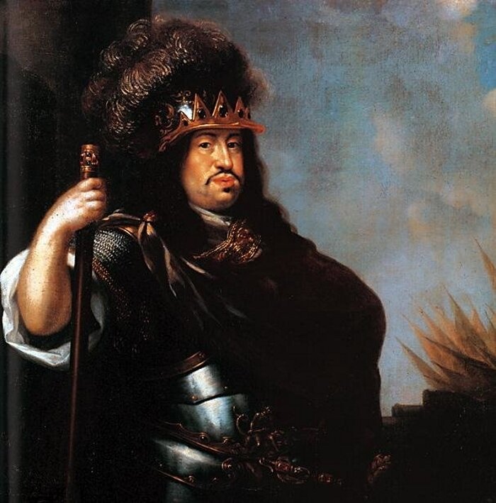 Obraz przedstawia Karola Dziesiątego Gustawa. Król ma długie czarne włosy, nosi wąsy. Ma na sobie zbroję.  W tle są armaty i wojskowe sztandary. 