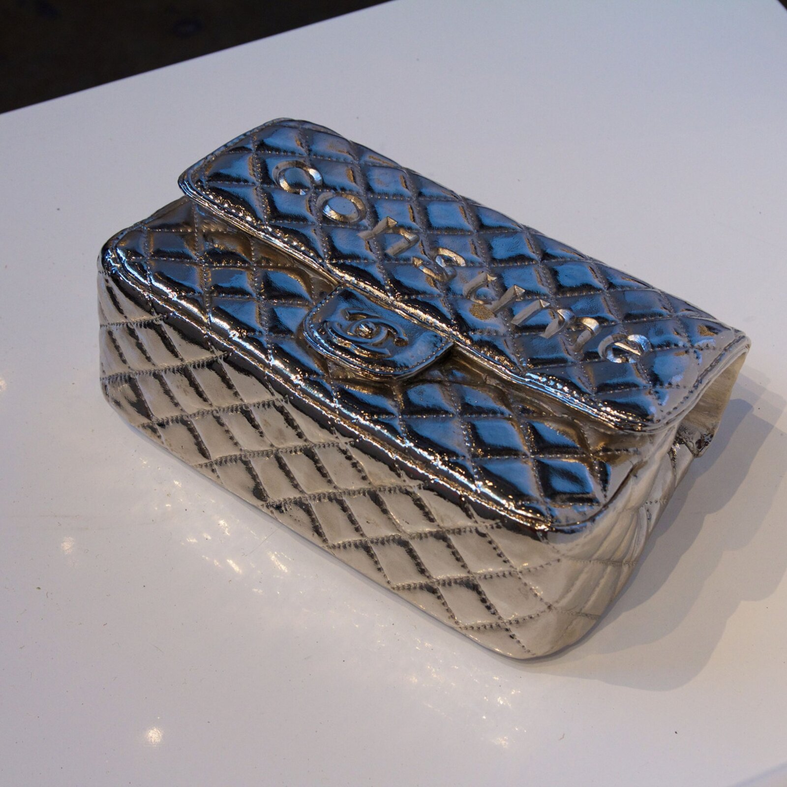 Ilustracja przedstawia pracę Willa Colesa  „Imitacja”. Ukazuje damską saszetkę wykonaną z brązu i powlekaną niklem. Przedmiot przeszywany jest w romby.