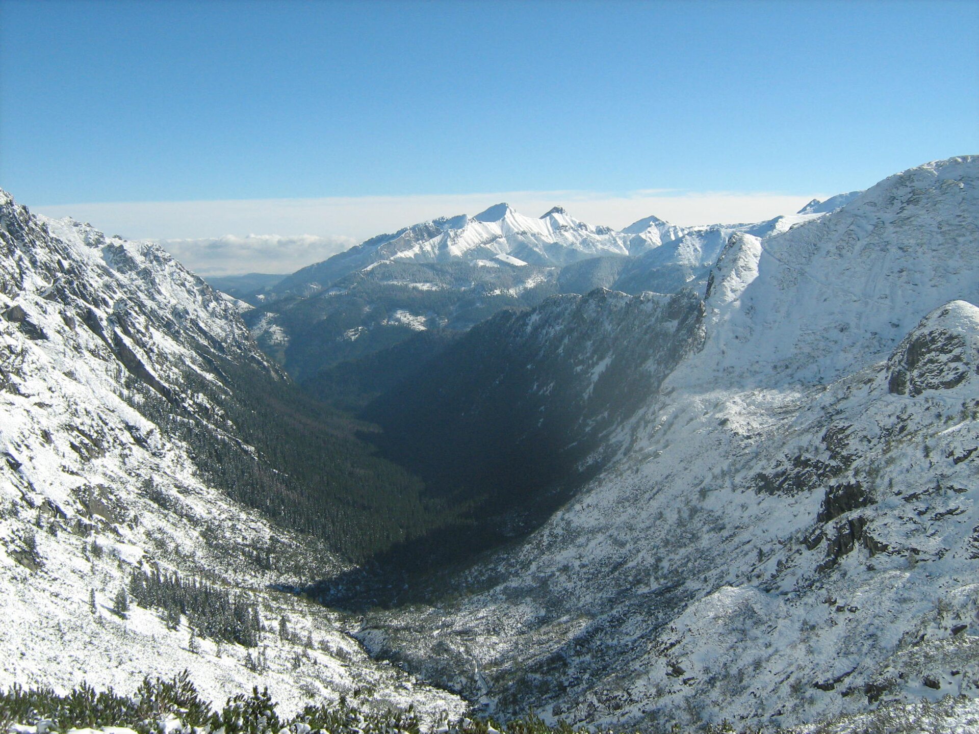 Fotografia prezentuje ośnieżone stoki górskie, które otaczają dookoła dolinę.