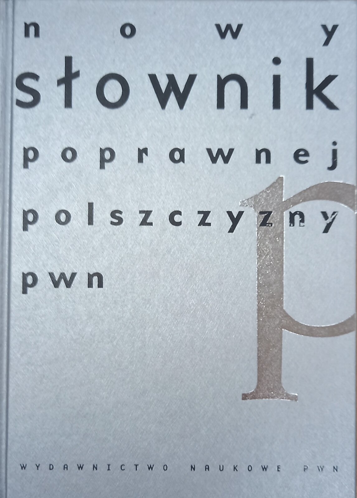 Kolorowa fotografia przedstawia okładkę Słownika poprawnej polszczyzny Wydawnictwa Naukowego PWN. Na szarym tle czarne litery. Treść napisu: nowy słownik poprawnej polszczyzny pwn. Na dole drukowanymi literami napis o treści: Wydawnictwo Naukowe PWN.