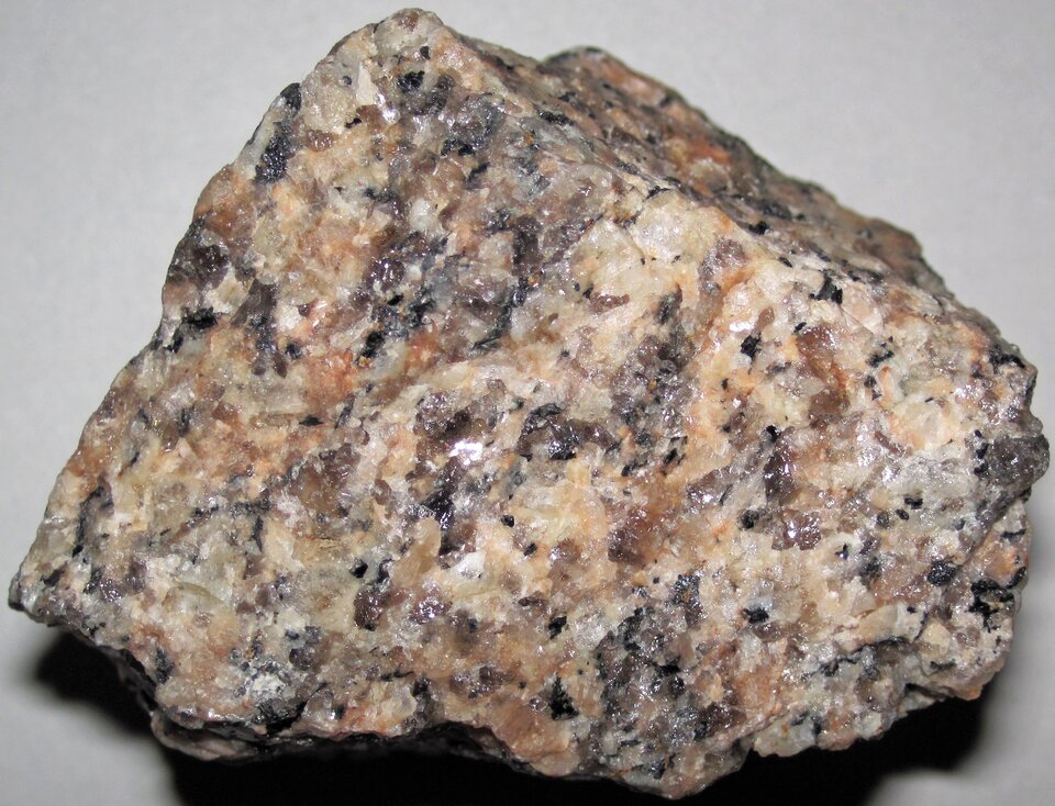 Zdjęcie przedstawia granit. Posiada ostre krawędzie oraz gładką, błyszczącą powierzchnię. Ma brązowo‑czarną barwę.