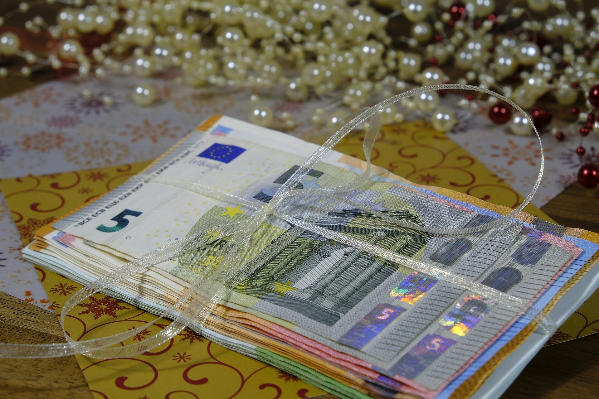 Na ilustracji widoczna jest niewielka sterta  banknotów euro rozłożonych na stole i przewiązanych ozdobną wstążką.