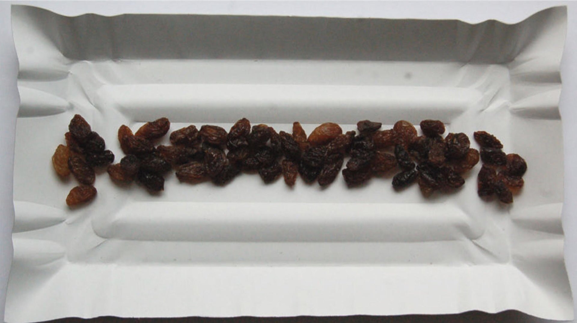 Rysunek do ćwiczenia 8 przedstawia fotografię papierowej tacki z leżącymi na niej rodzynkami. Widok z góry.