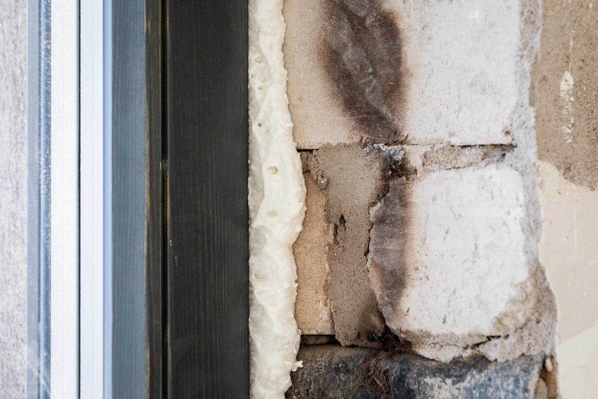 Zdjęcie przedstawia uszkodzenia izolacji termicznej elewacji. Widać ciemne uszkodzenie izolacji.