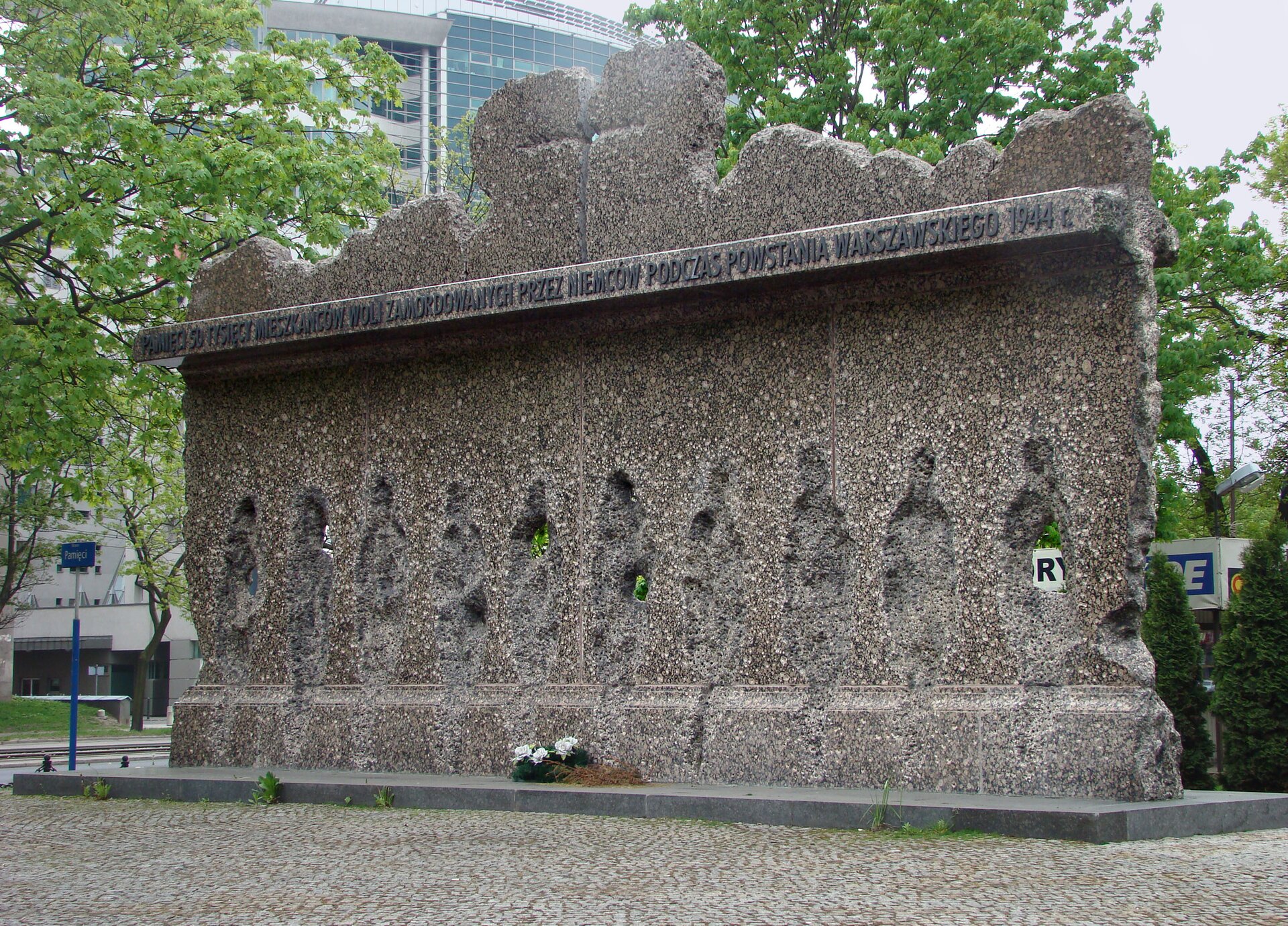 Zdjęcie przedstawia pomnik stworzony poprzez wyżłobienie dziur w kształcie ludzi w kamiennej skale. Górę pomnika wieńczy wyszczerbiony, nierówny mur.